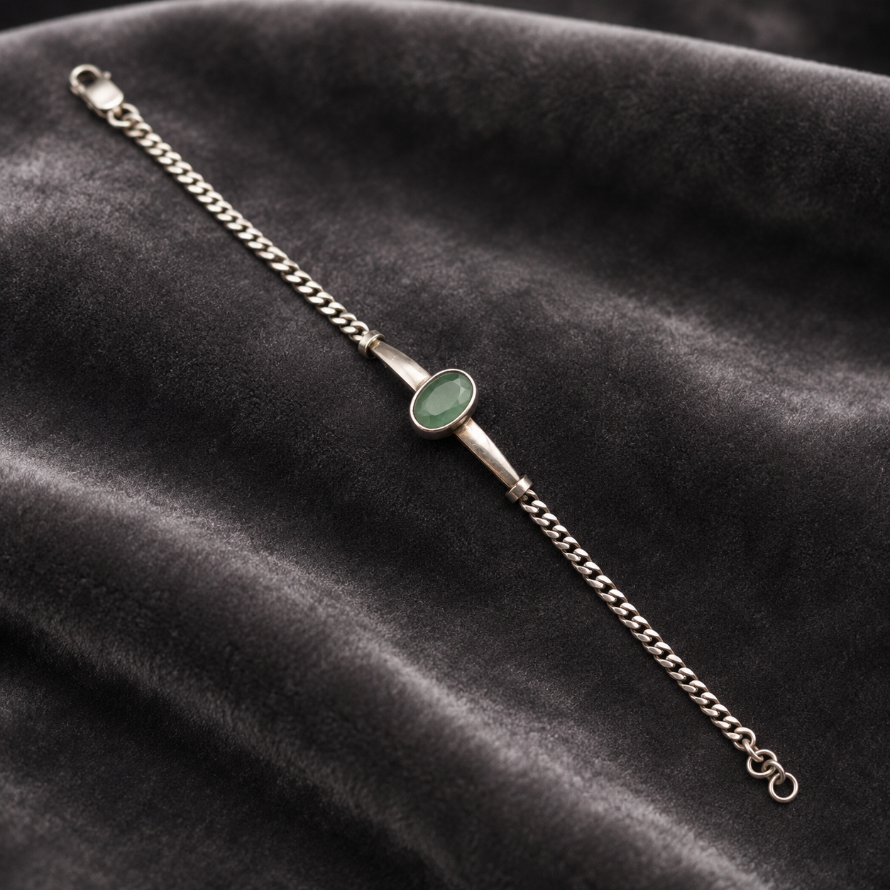 Silver bracelet with green emerald panna center and chain clasp on dark velvet