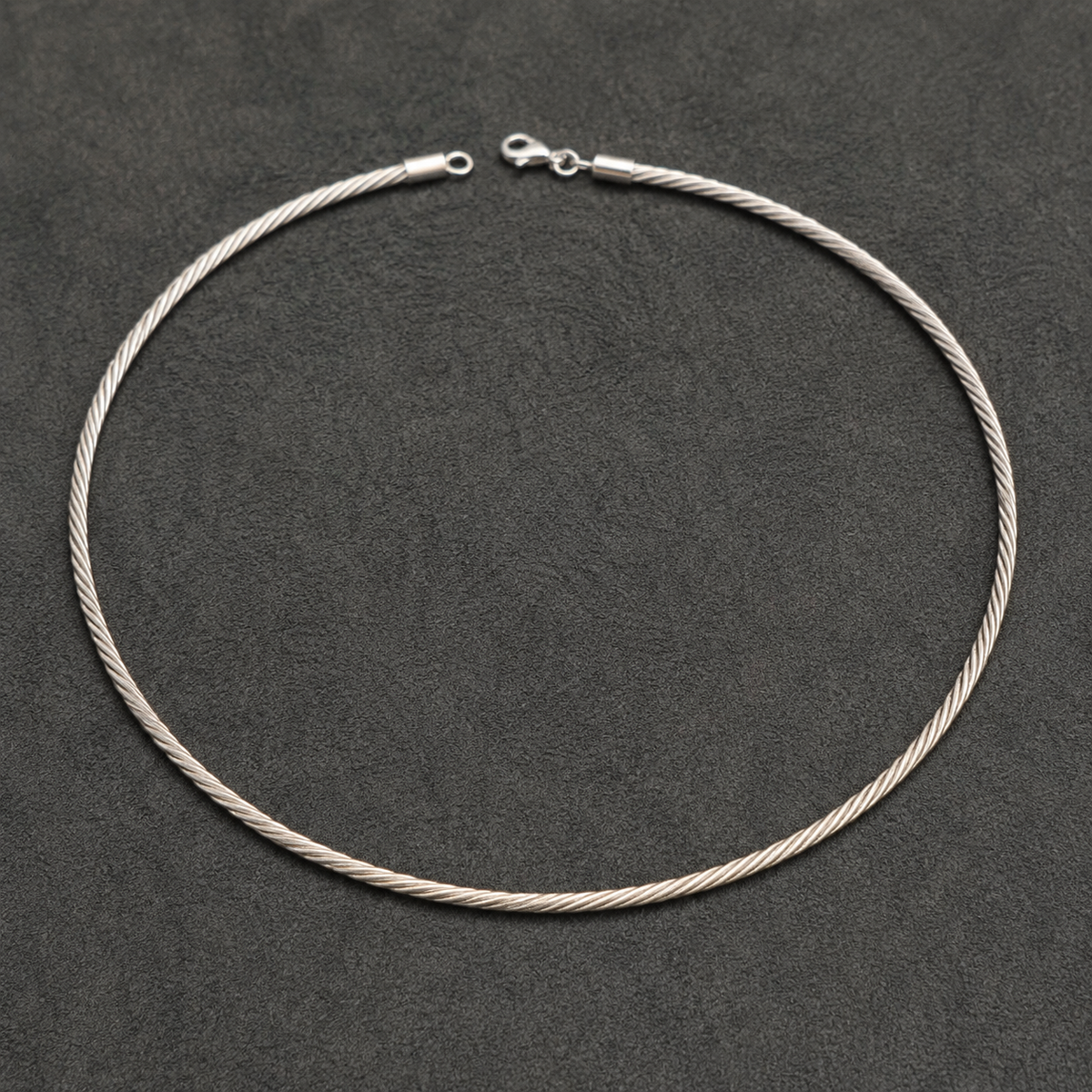 Silver Italian-style twisted hasli necklace with clasp and chain links laid on dark background