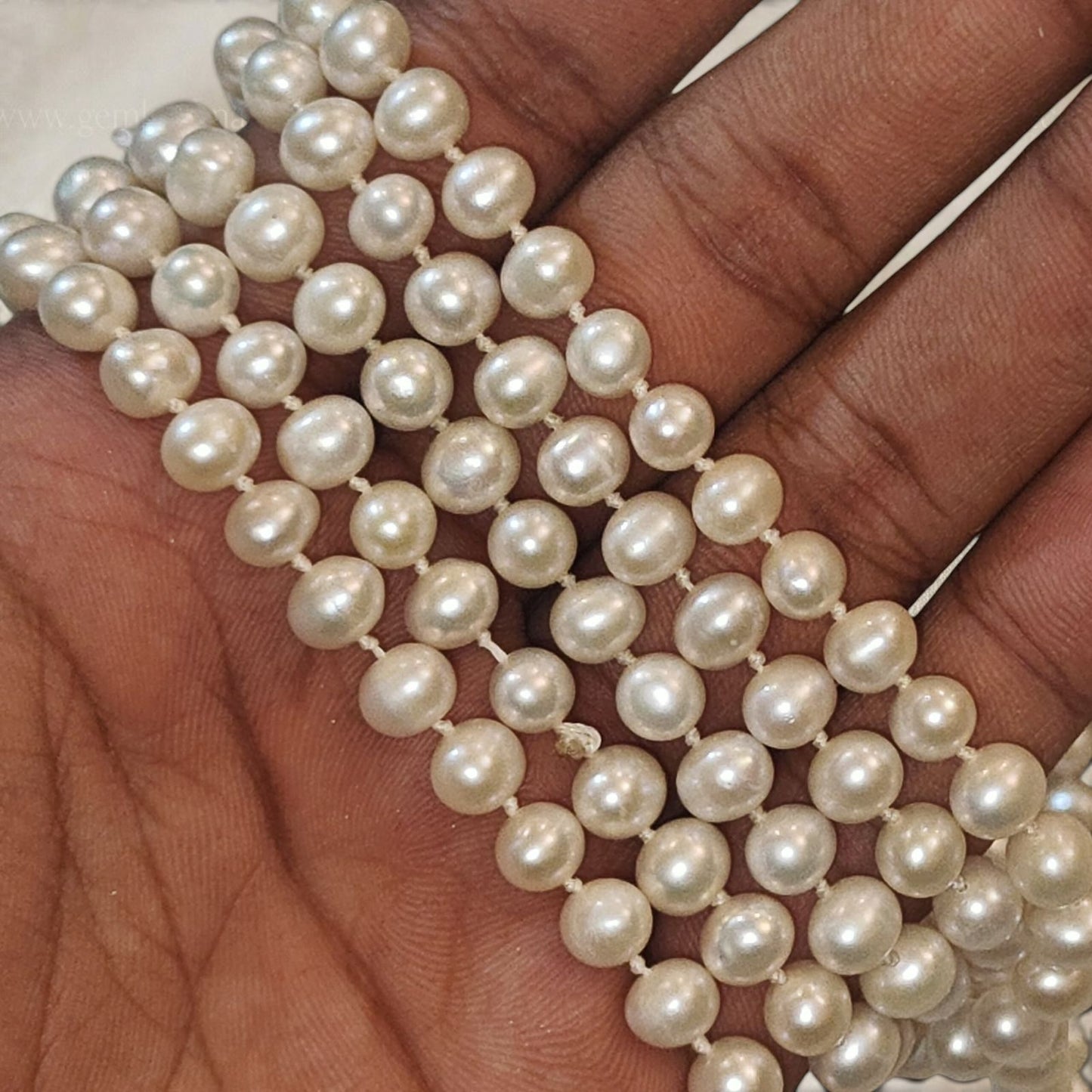 Strand of round pearl beads with cream luster, held in hand for jewelry making