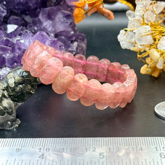 Strawberry quartz flat oval bead bracelet laid flat on black surface with ruler