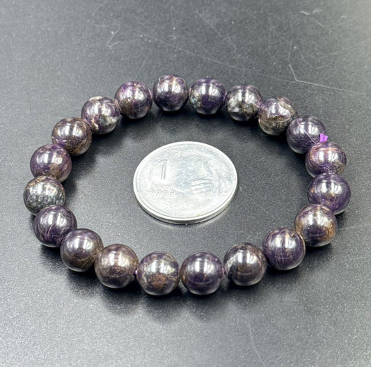 Sugilite beaded bracelet with purple round stones shown beside a coin for size