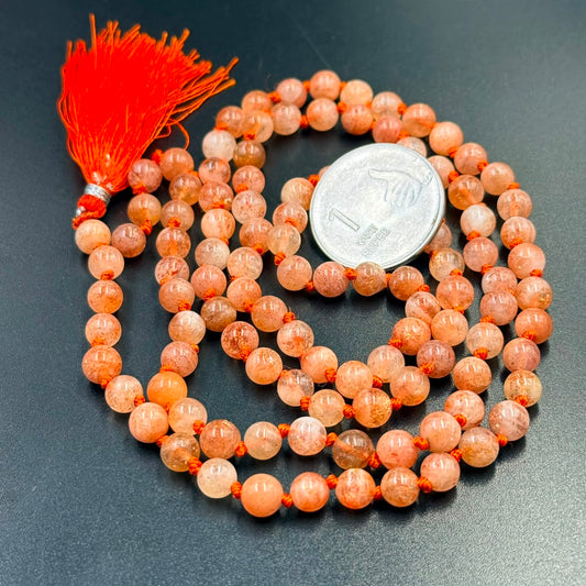 Close-up of sunstone mala 6mm orange bead bracelets with red tassel and coin for scale