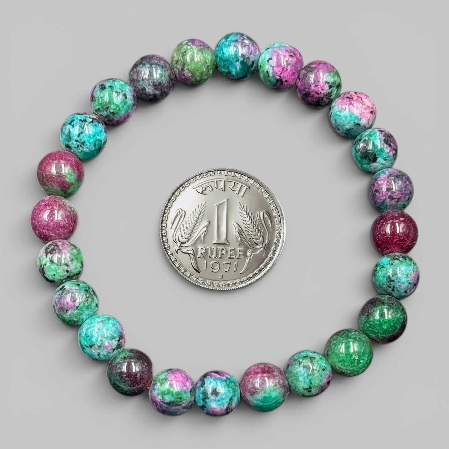 Synthetic ruby zoisite bracelet beads with coin for scale, heart charm not visible