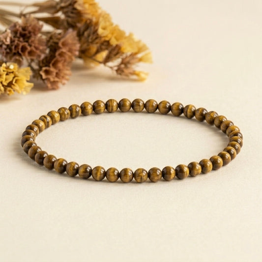 Tiger's eye bracelet laid flat with round beads and dried flower accent on light background