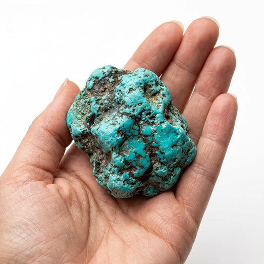 Dyed turquoise howlite raw crystal held in open hands, showing blue-green matrix texture