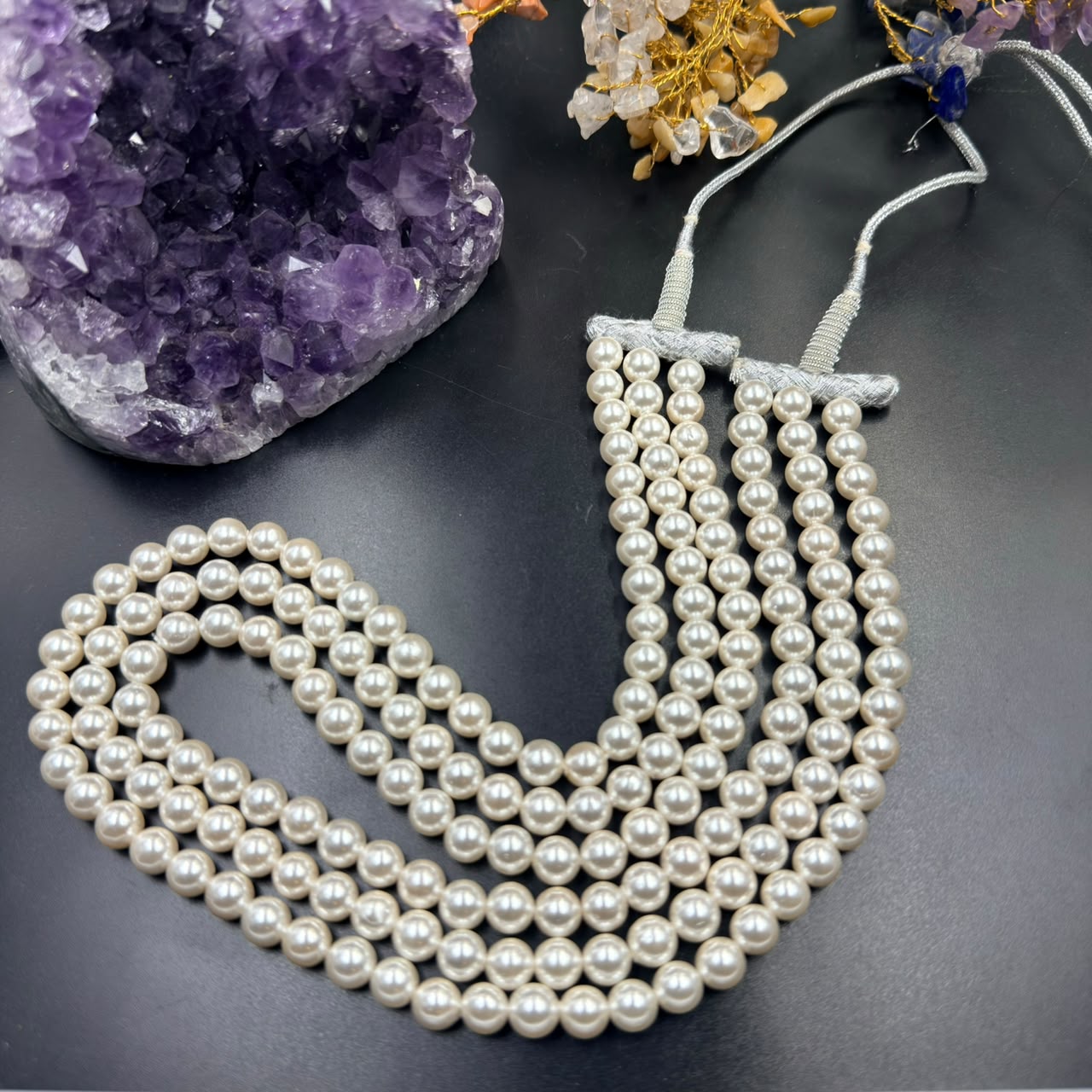 White pearl 3-layer mala necklace laid flat with tassel strings over dark background