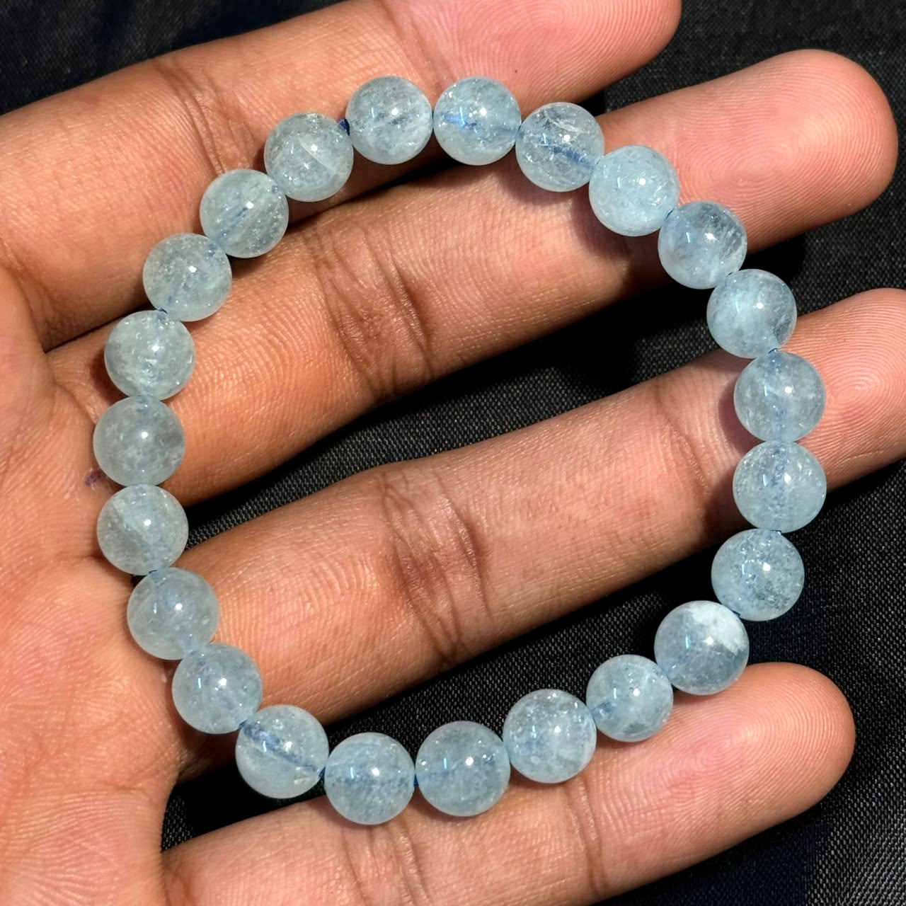 Light blue round aquamarine beads strung as a bracelet held in hand against black background