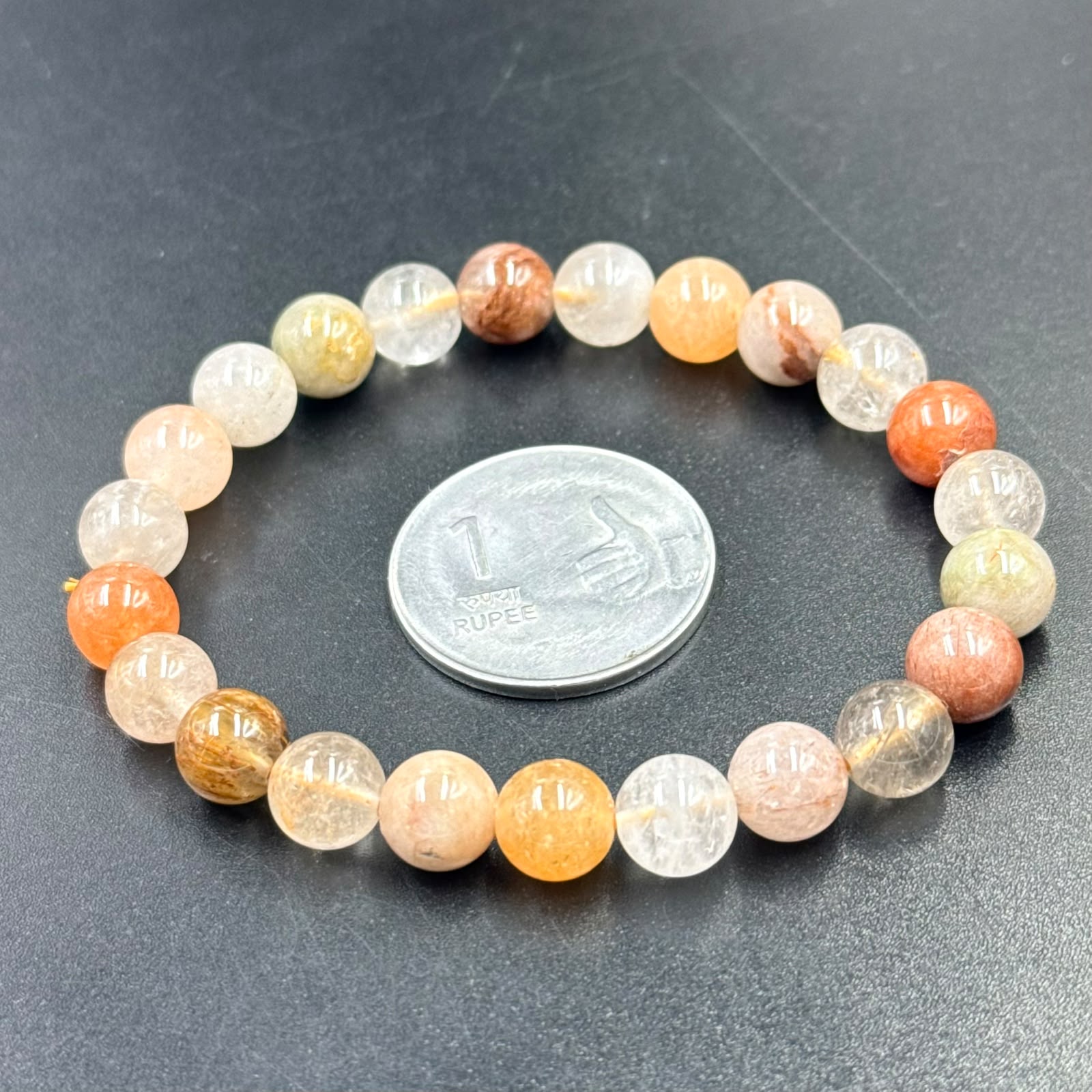 Lodolite Bracelet with multicolored round beads displayed beside a 1 rupee coin on a black surface