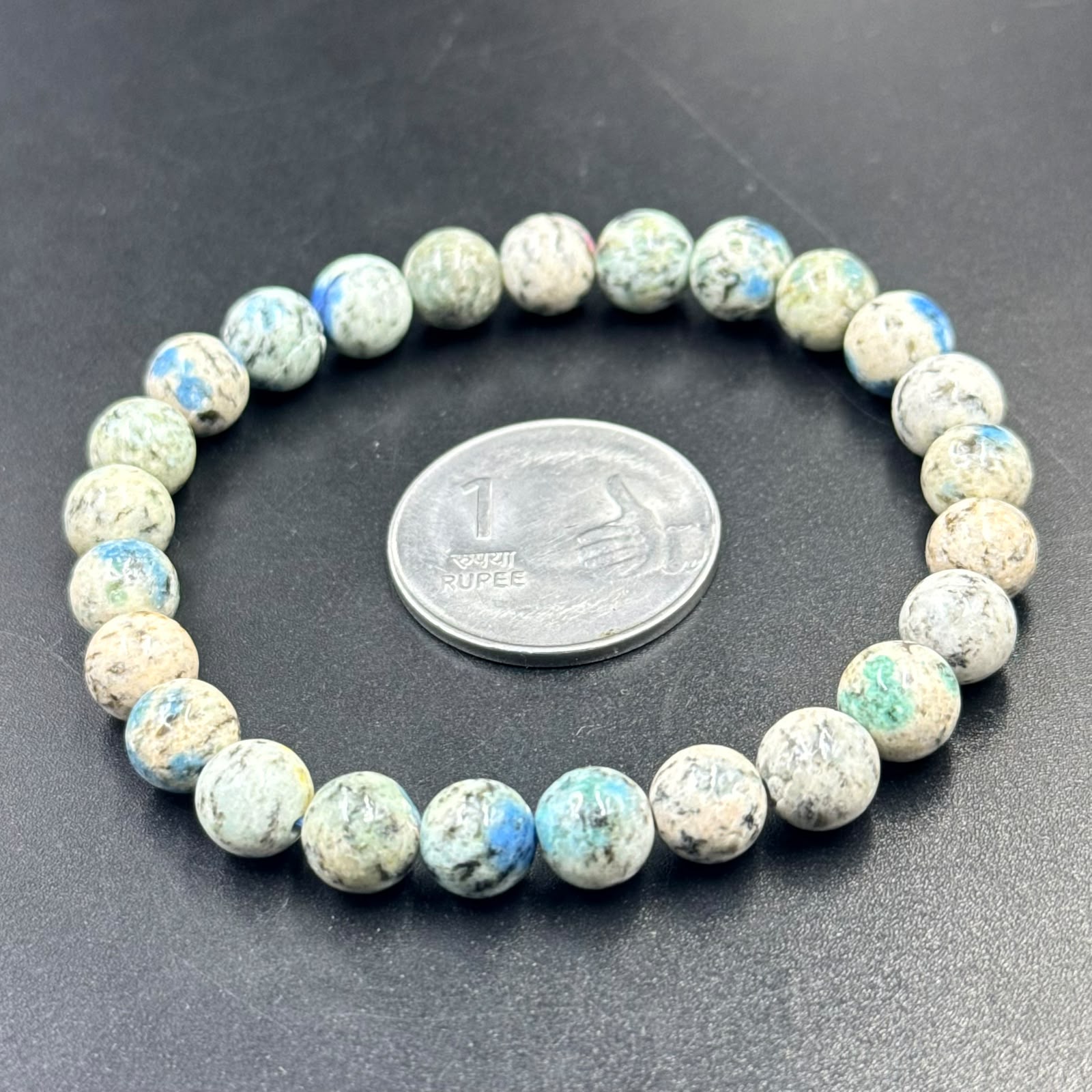 K2 Jasper Bracelet beads arranged in a circle with a 1 rupee coin on a black surface
