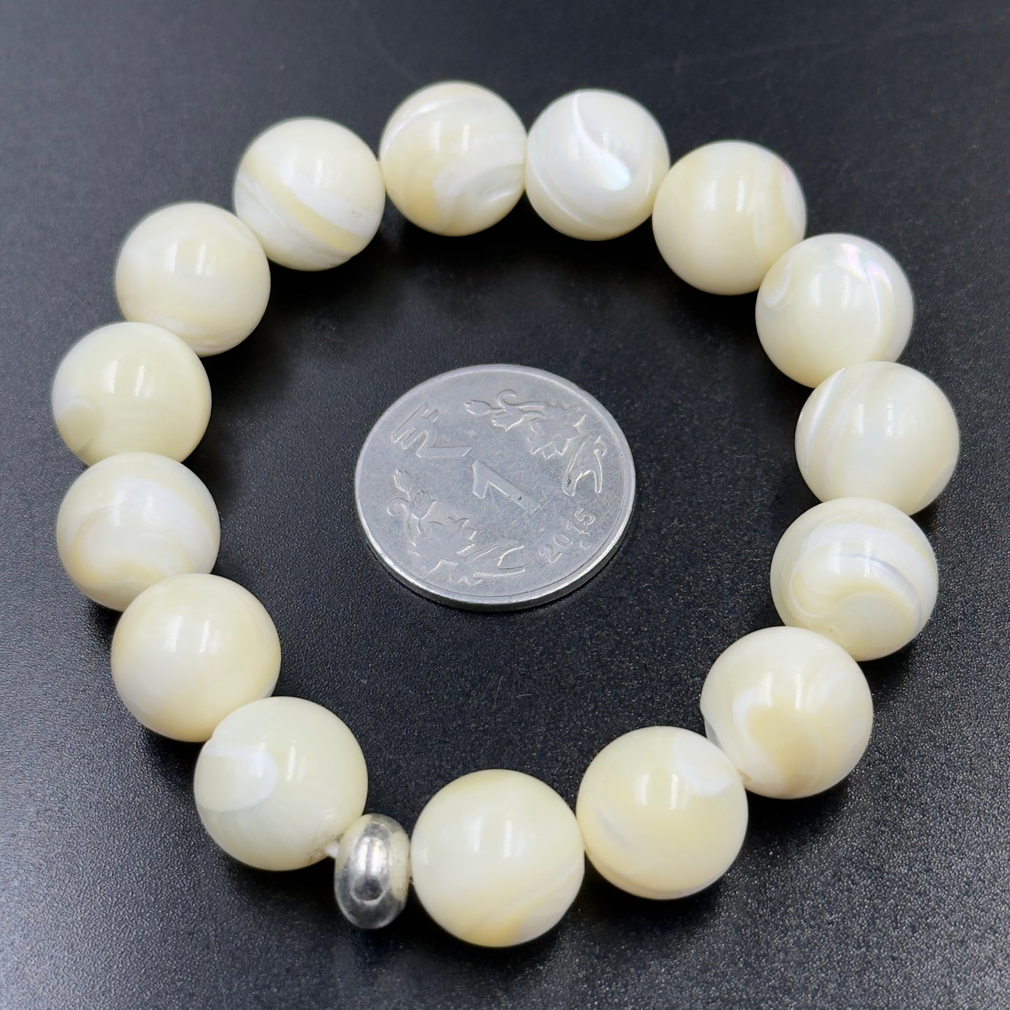 Mother of Pearl Bracelet with round cream beads and one silver spacer bead, next to a coin.