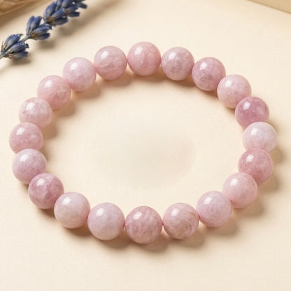 Pink Kunzite Bracelet with round polished beads arranged in a circle on beige surface with dried lavender sprig nearby