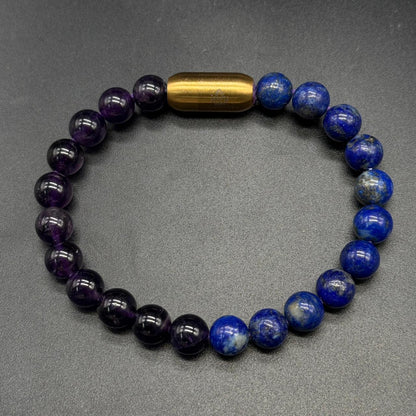 A beaded bracelet made of alternating dark purple amethyst and deep blue lapis lazuli ball beads, with a polished gold cylindrical accent bead at the top, displayed on a dark gray textured background  custom bracelet by GemKrishna