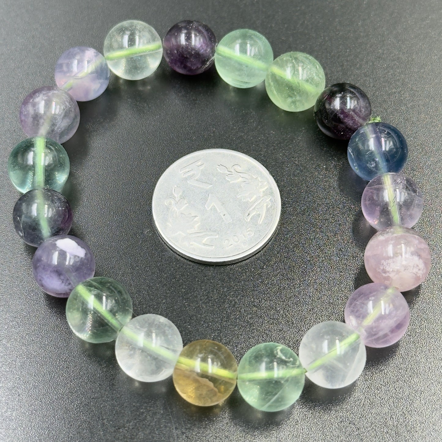 Multi Fluorite Bracelet with round translucent beads in various green, purple, blue, and yellow shades next to a coin
