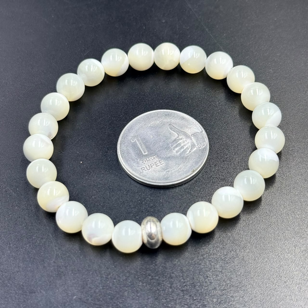 Mother of Pearl Bracelet with round beads and single silver spacer bead next to a 1 rupee coin on black surface