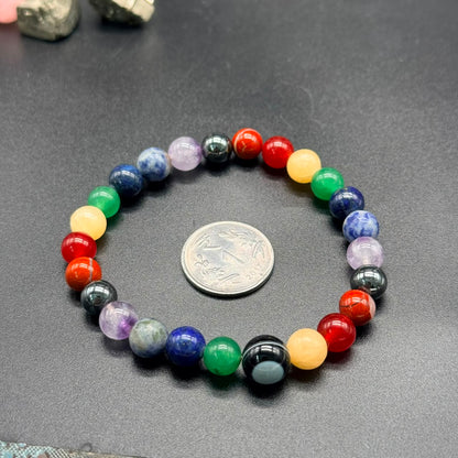 7 Chakra Balance Bracelet with multicolored round beads arranged in a circle next to a coin on a black surface