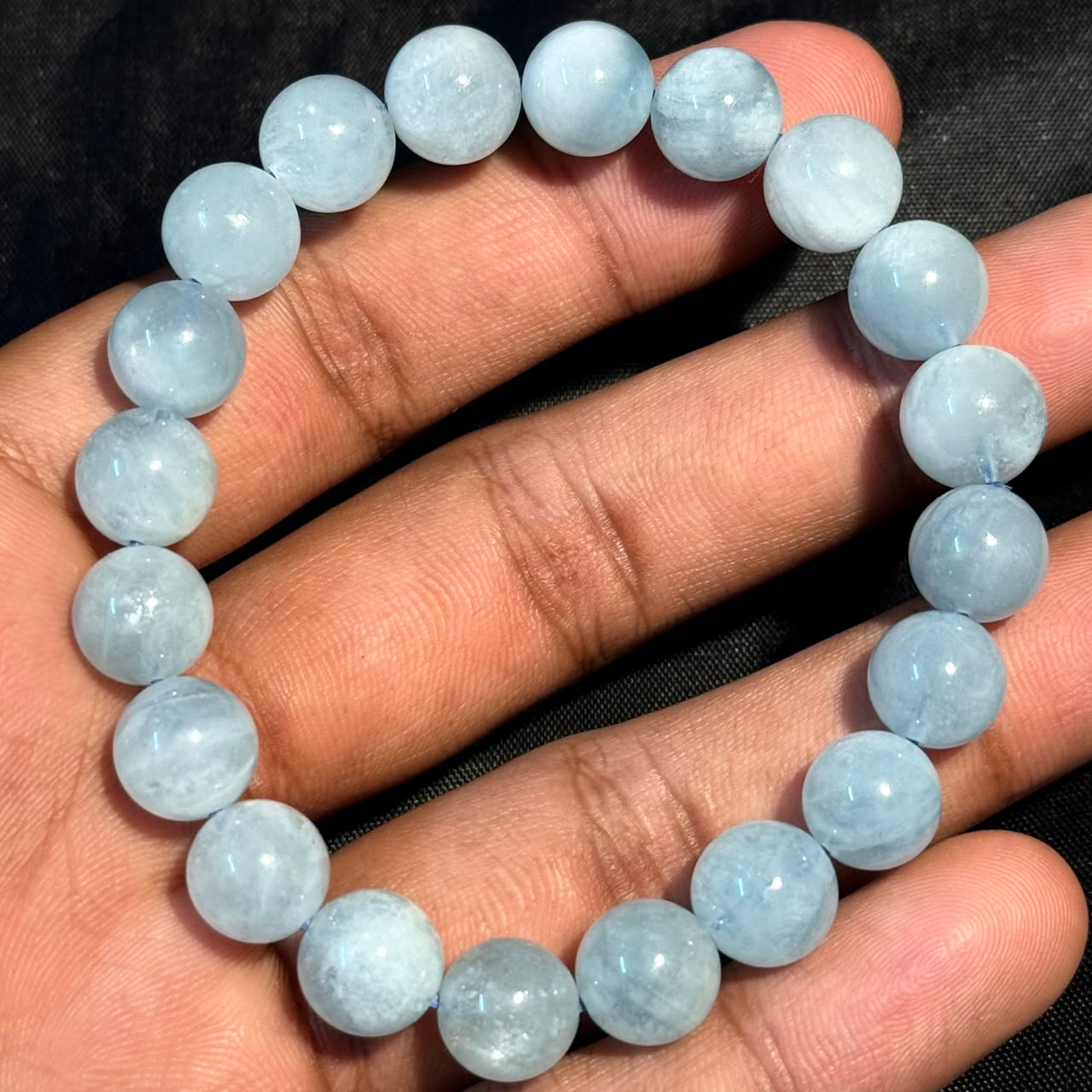 Aquamarine Bracelet held in hand showing round pale blue beads strung on elastic cord