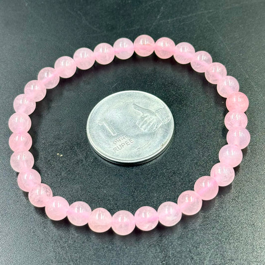 Rose Quartz AAA 6mm Bracelet with round pink beads surrounding an Indian one rupee coin on black surface