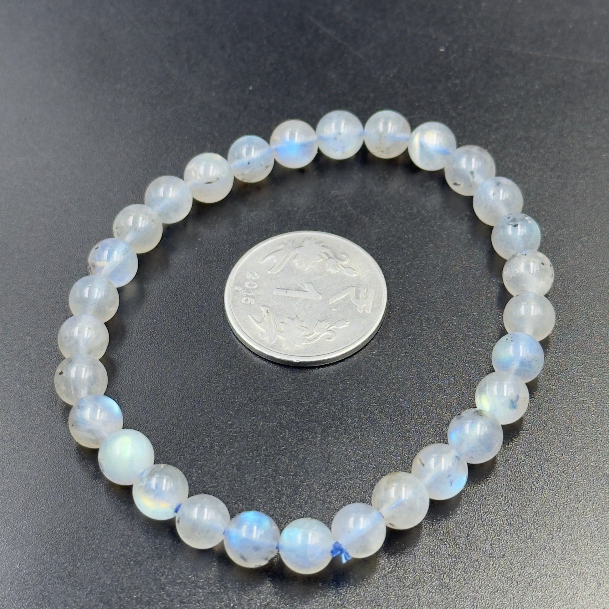 Labradorite Bracelet with round translucent beads showing blue flashes, placed around a coin on black surface