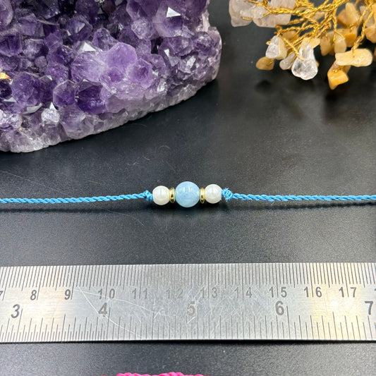 Aquamarine & Pearl Crystal Rakhi Bracelet with blue thread and gold spacers on black surface with ruler