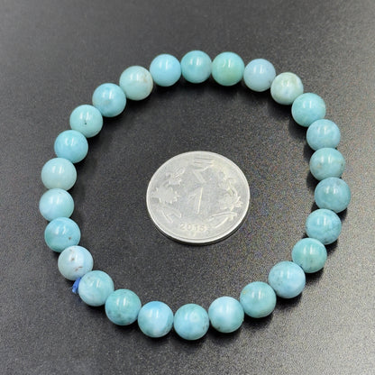 Larimar Bracelet with round blue beads arranged in a circle around an Indian one-rupee coin on a dark surface