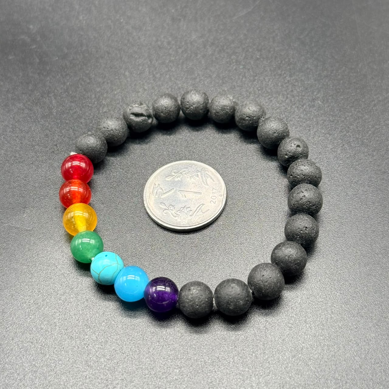 7 Chakra Balance Bracelet with seven colored beads and black textured beads, displayed next to a coin.