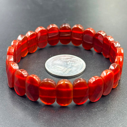 Carnelian flat oval bead bracelet displayed in a circle next to a 1 rupee coin on a dark surface