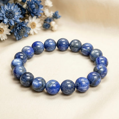 Blue Kyanite Bracelet with polished round beads on a beige fabric background with dried blue and white flowers