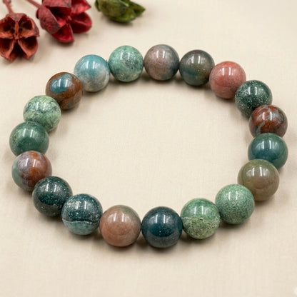 Round multicolored Bloodstone beads arranged in a circular bracelet on a beige background