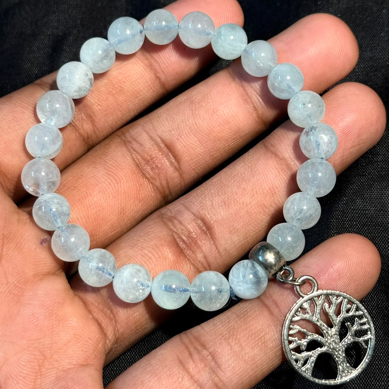 Aquamarine Bracelet with round beads and silver Tree of Life charm held on hand against black background