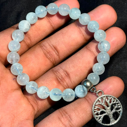 Aquamarine Bracelet with round beads and silver Tree of Life charm held on hand against black background