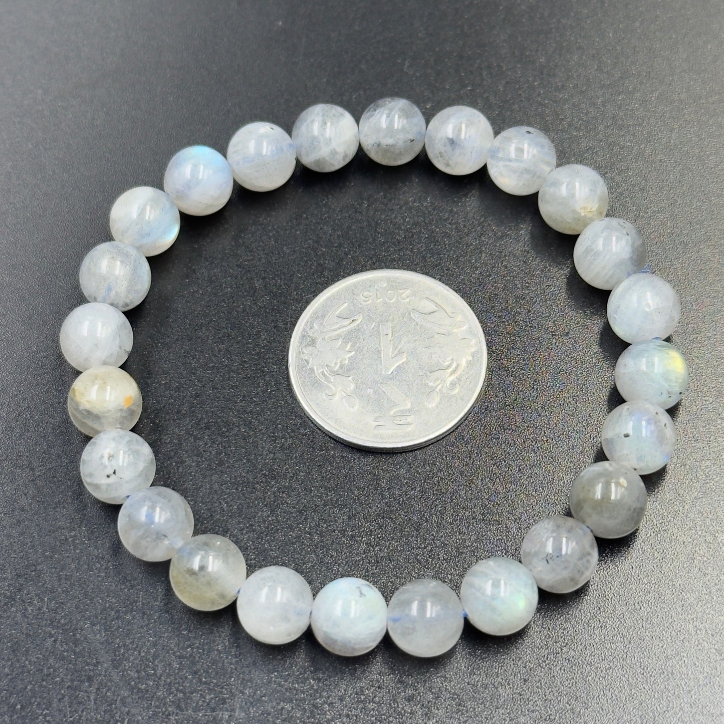 Round labradorite bead bracelet encircling a silver coin on a dark surface