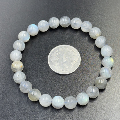 Round labradorite bead bracelet encircling a silver coin on a dark surface