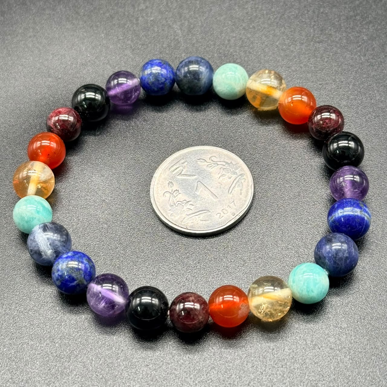 7 Chakra Balance Bracelet with multicolored round beads arranged in a circle around a coin on black surface