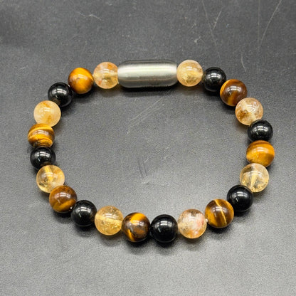 A beaded bracelet with alternating black tourmaline and tiger's eye beads, Citrine  crystals, and a central metallic silver lock magnetic , displayed on a dark gray textured surface.