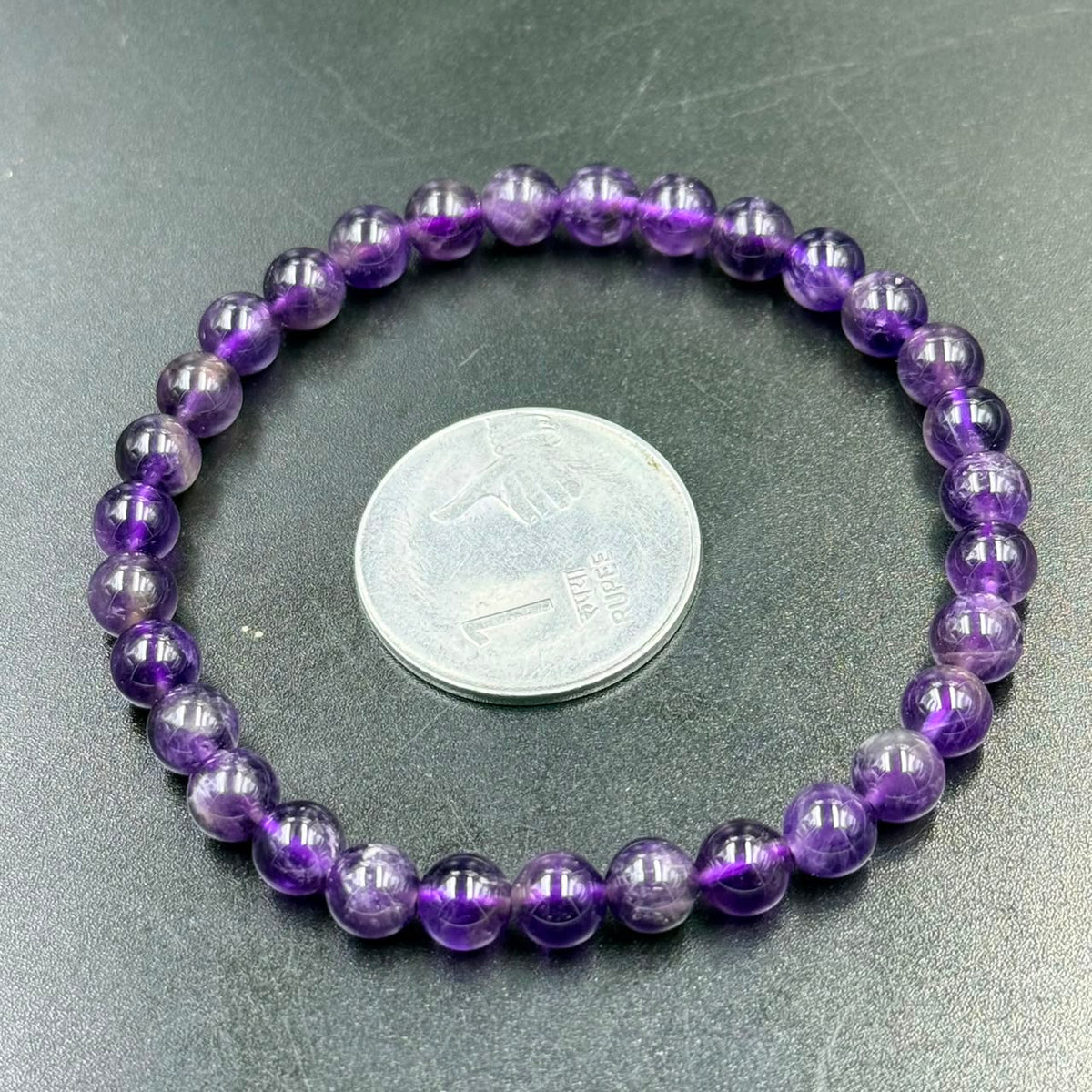 Close-up of 6mm amethyst bead bracelet resting on a green surface with coin for scale