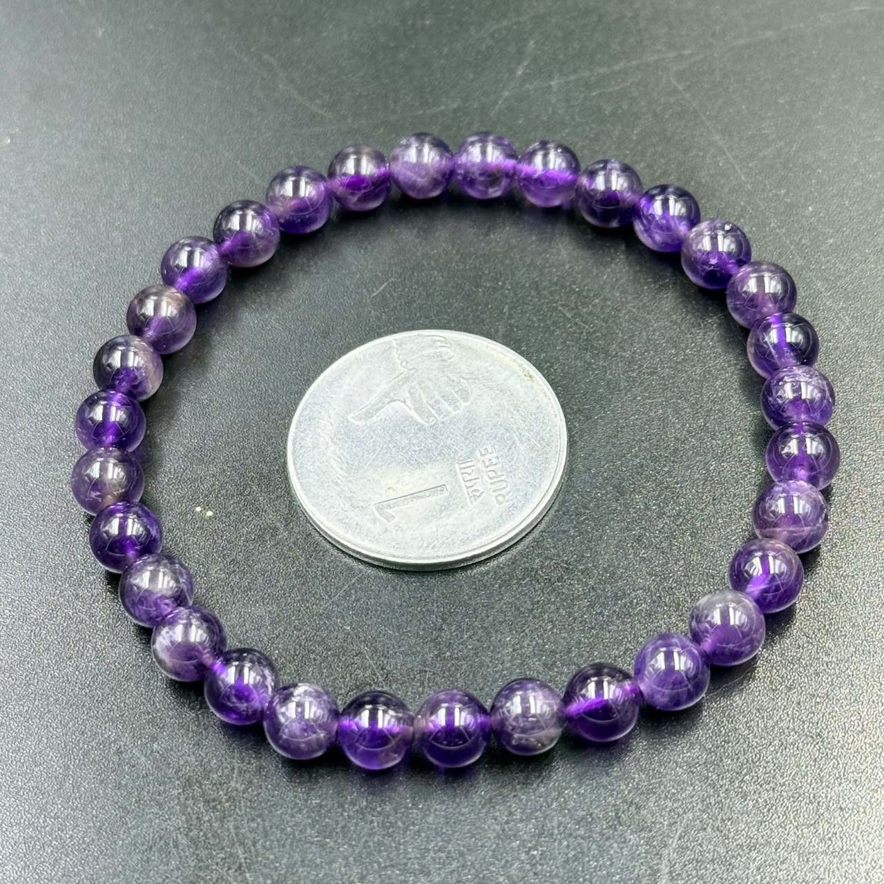Close-up of 6mm amethyst bead bracelet resting on a green surface with coin for scale