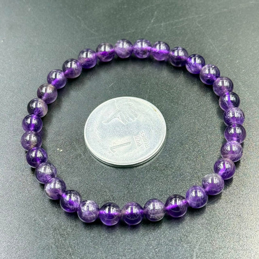 Close-up of 6mm amethyst bead bracelet resting on a green surface with coin for scale