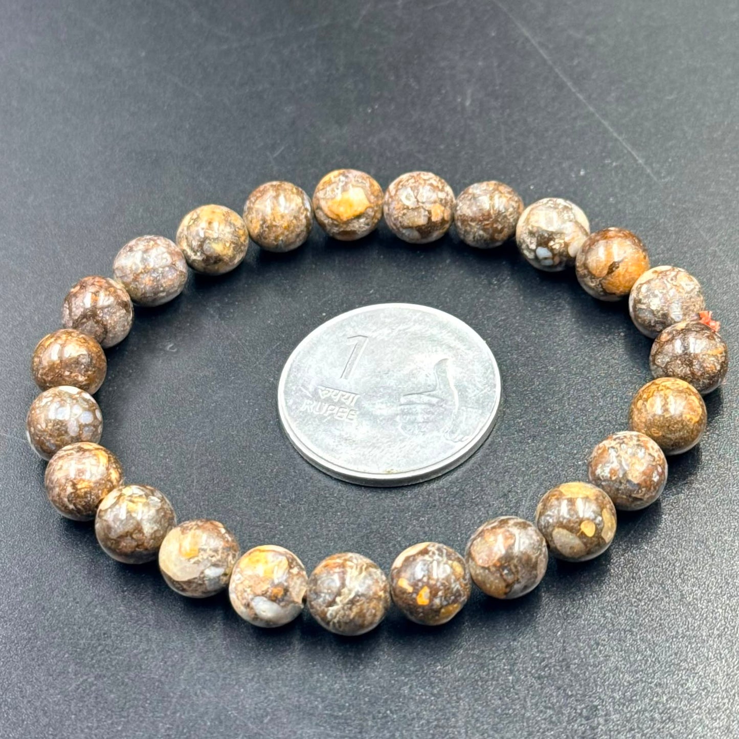 African Lace Opal Bracelet with round brown and beige patterned beads next to a one rupee coin