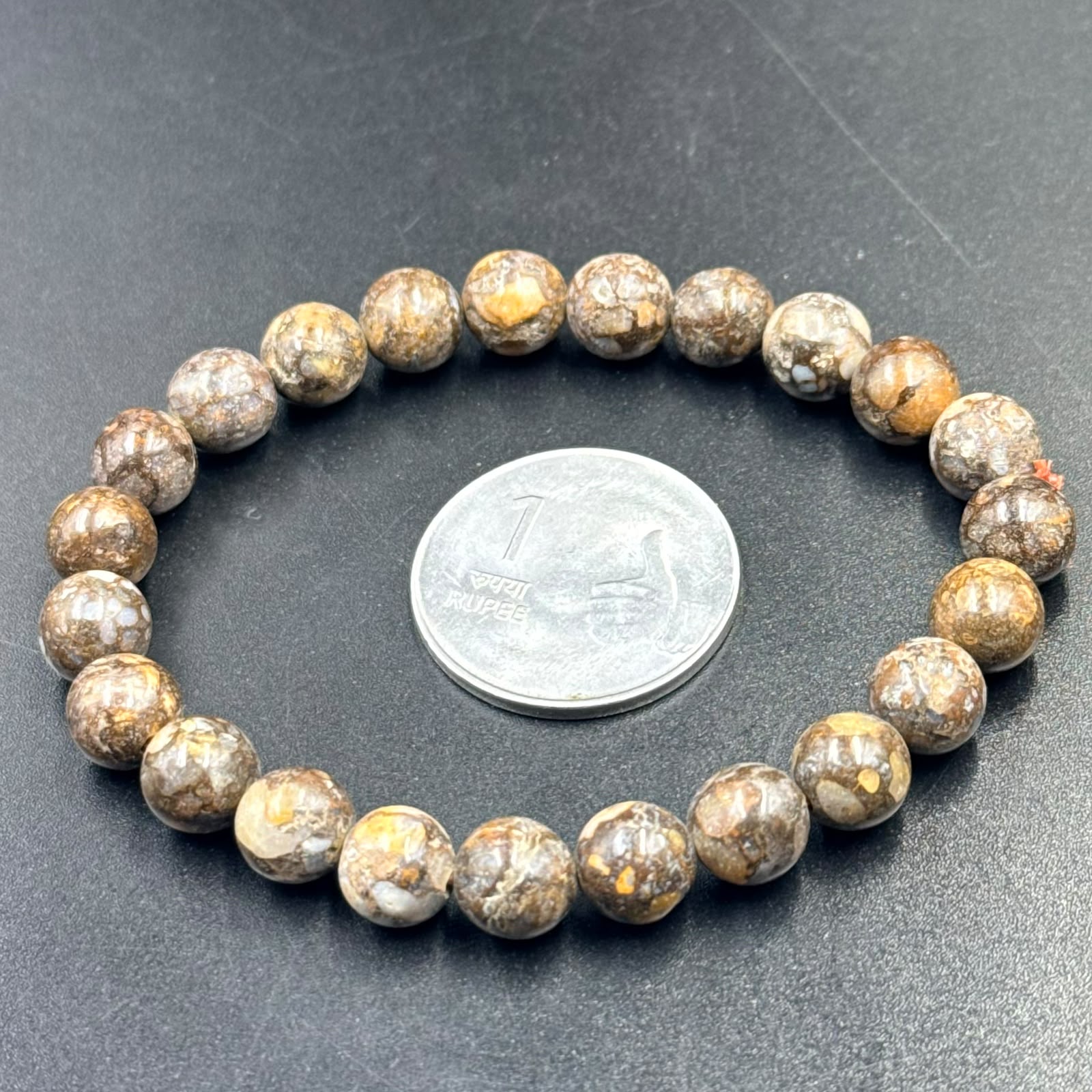 African Lace Opal Bracelet with round brown and beige patterned beads next to a one rupee coin