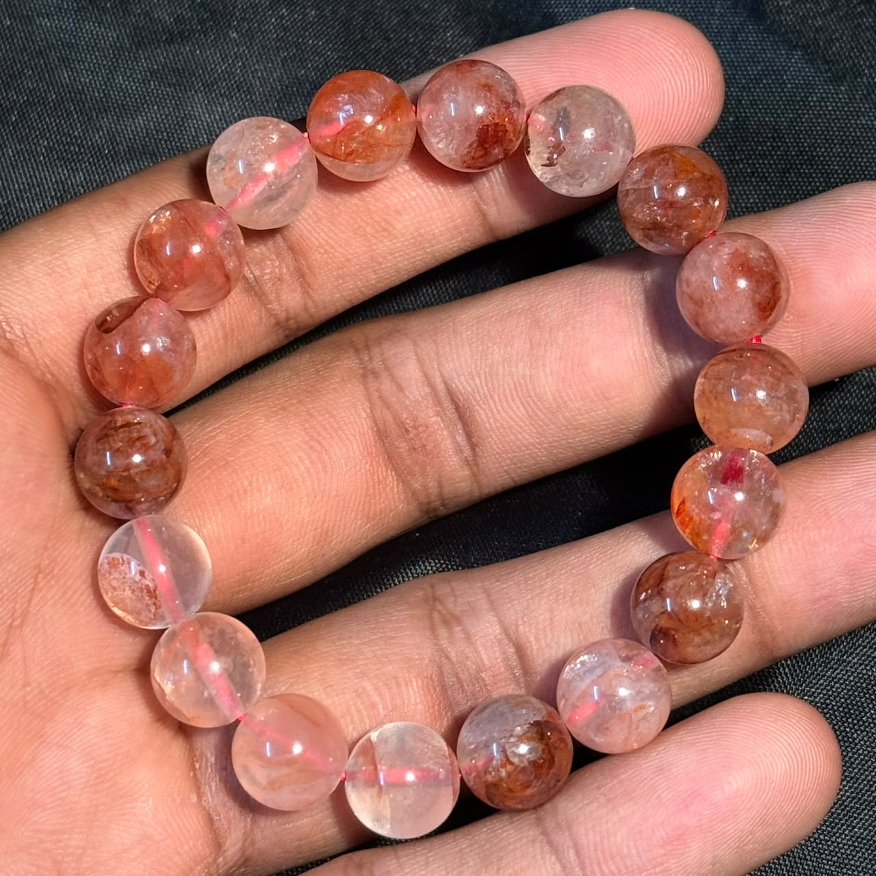 Hematoid Quartz/Lepidocrocite bracelet with round translucent beads in a hand on black background