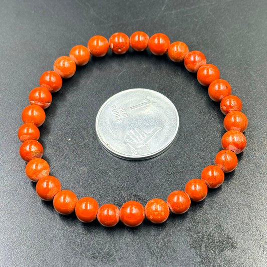 Red Jasper 6mm Bracelet with round orange beads placed beside an Indian 1 rupee coin on black surface