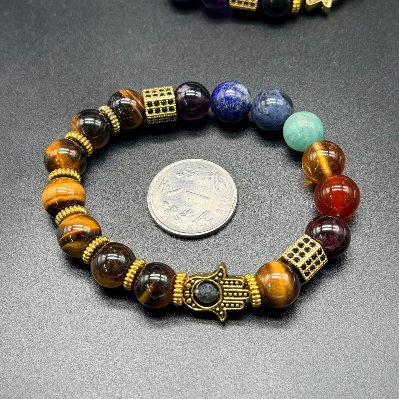 7 Chakra Balance Bracelet with multicolored beads and gold-tone accents, next to a coin for size comparison