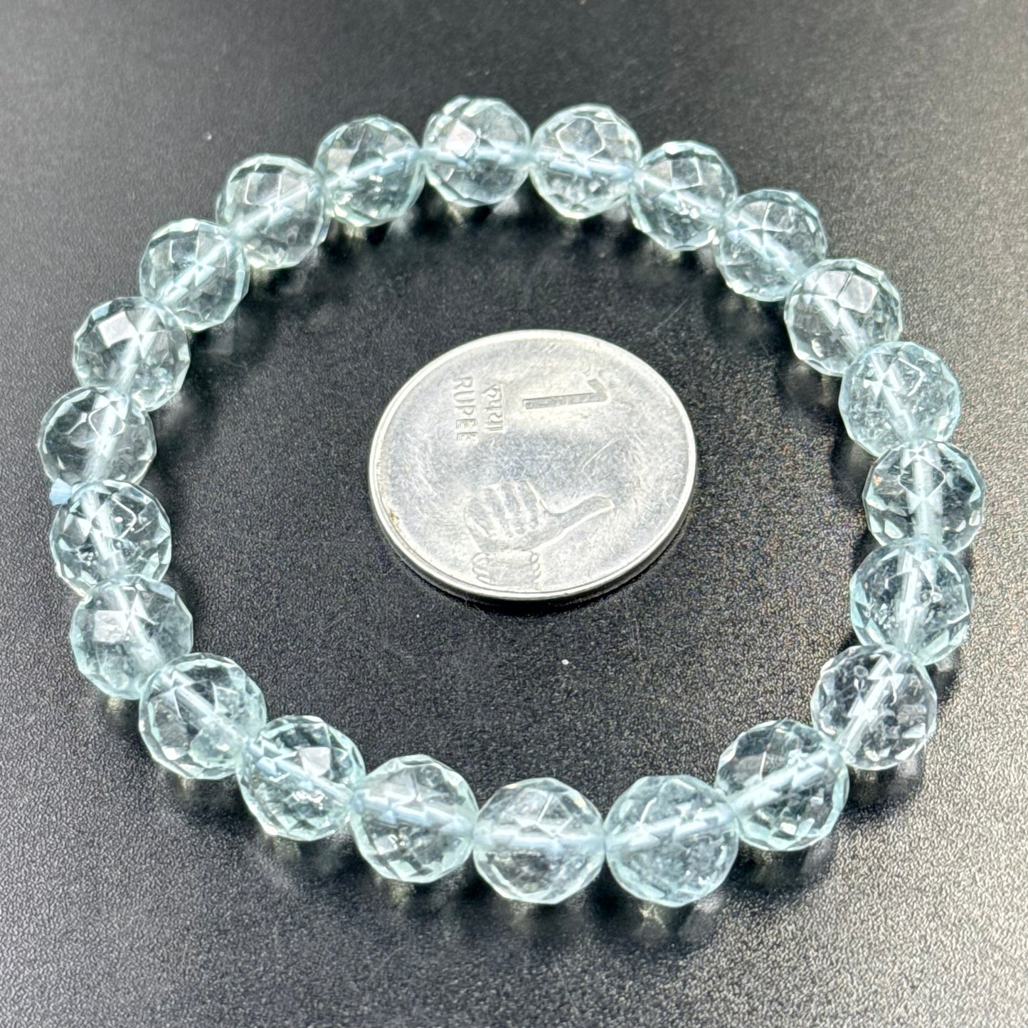 Blue Topaz Bracelet with faceted round beads displayed next to one rupee coin on black surface