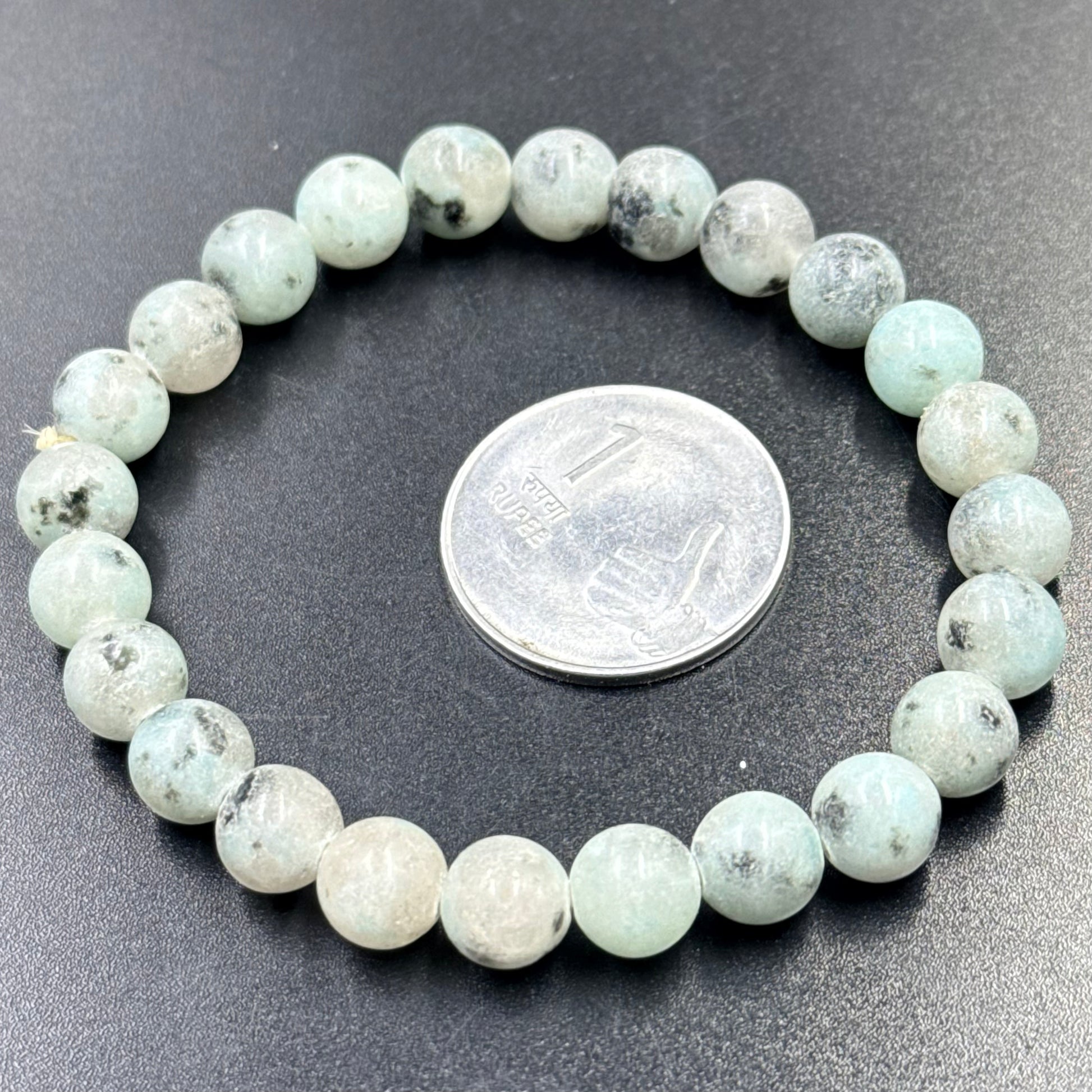 Kiwi Jasper Bracelet with round beads arranged in a circle beside an Indian 1 rupee coin on black surface