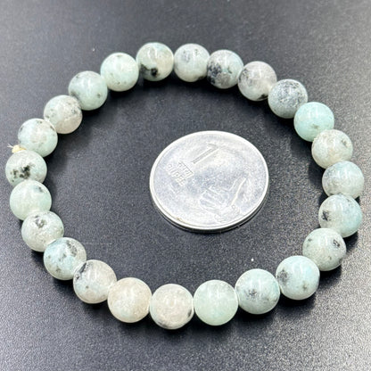 Kiwi Jasper Bracelet with round beads arranged in a circle beside an Indian 1 rupee coin on black surface