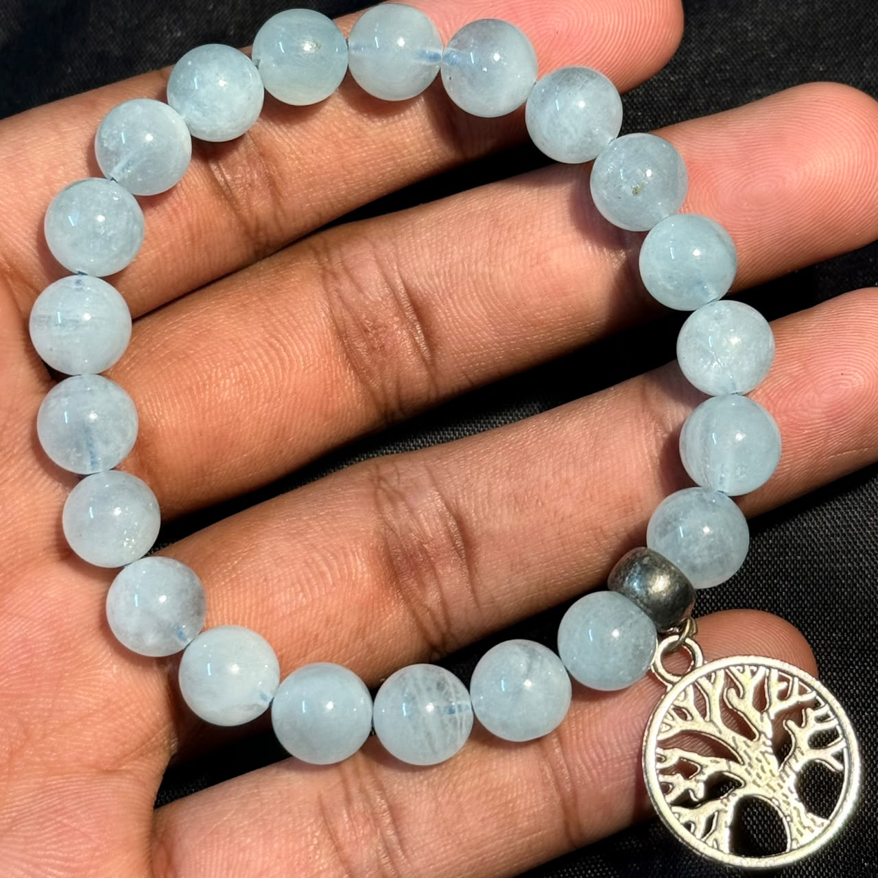 Aquamarine bracelet with round beads and a silver tree of life charm held in hand