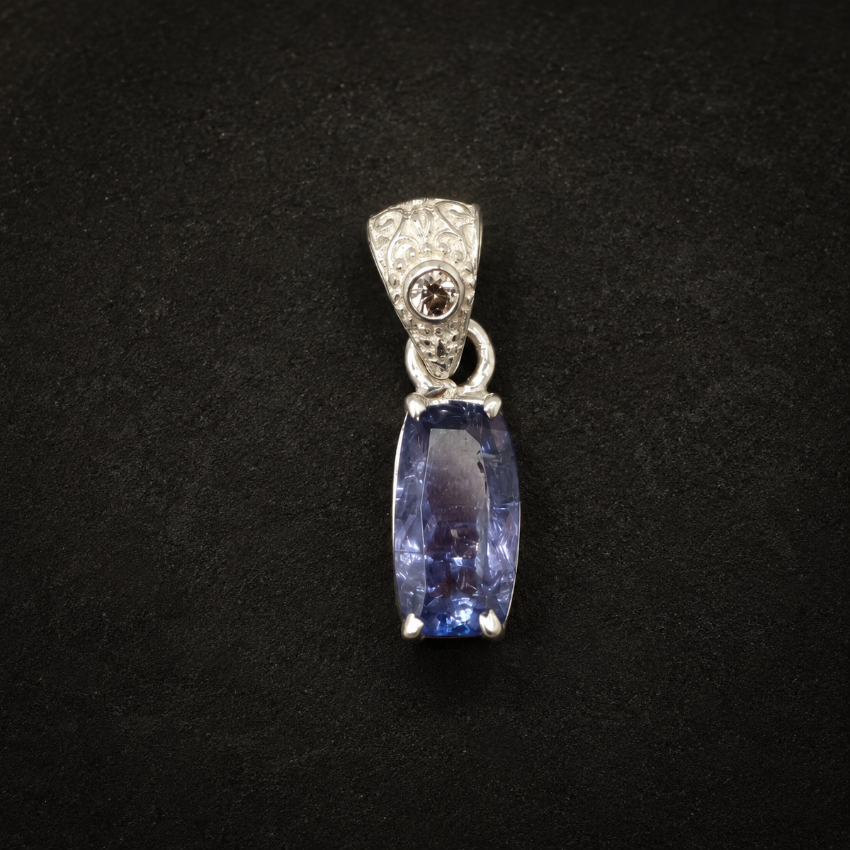 Natural tanzanite and lab-grown diamond pendant front view on black textured background