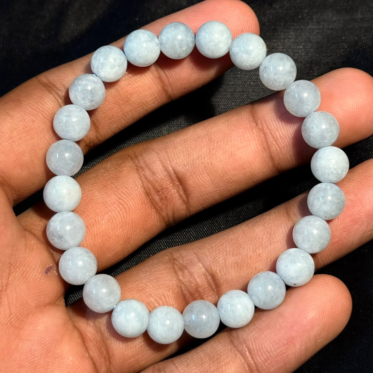 Aquamarine Bracelet with smooth round beads held on fingertips against dark background