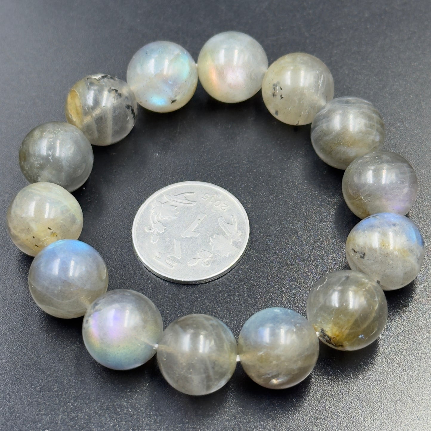 Labradorite bracelet with round beads showing flashes of blue and multicolor on black surface with coin