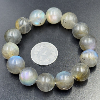Labradorite bracelet with round beads showing flashes of blue and multicolor on black surface with coin